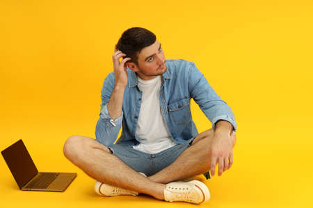 Young man and laptop on yellow background.の写真素材