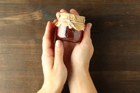 Female hands hold a jar of raspberry jam on wooden backgroundの写真素材