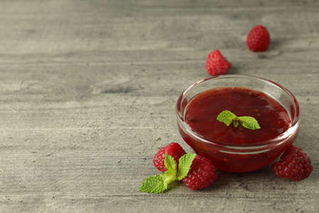 Glass bowl of raspberry jam with ingredients on gray textured backgroundの写真素材
