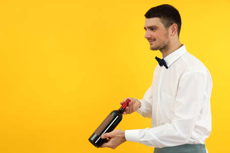 Young man waiter holds bottle of wine on yellow background.の写真素材