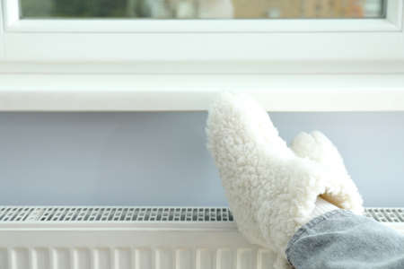 Concept of heating season with legs in knitted boots on radiator.