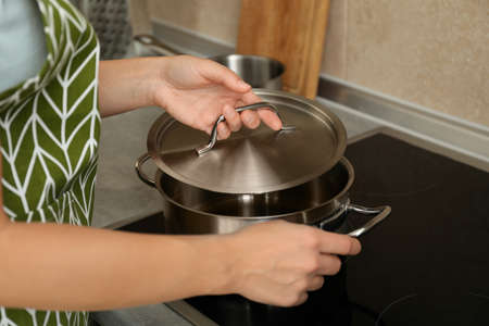 Woman in apron holds metal pot and pot cap.の写真素材
