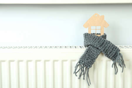 Concept of heating season with wooden house on heating radiator.