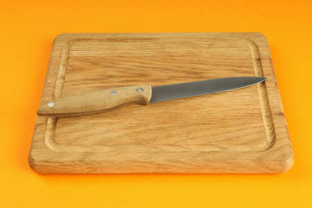 Cutting board with knife on orange background.