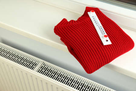 Concept of heating season with sweater with thermometer on windowsill.の写真素材