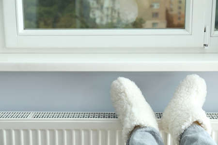 Concept of heating season with legs in knitted boots on radiator.
