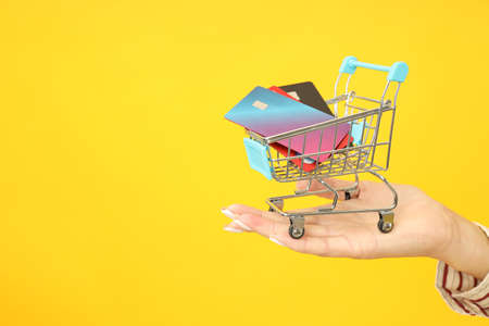 Female hand holds shop trolley with credit cards on yellow background.の写真素材
