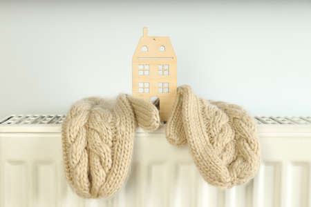 Concept of heating season with mittens and wooden house on radiator.の写真素材