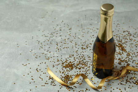 Bottle of champagne, glitter and ribbon on gray texture background.の写真素材