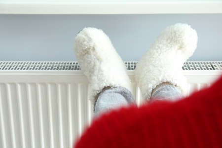Concept of heating season with legs in knitted boots on radiator.