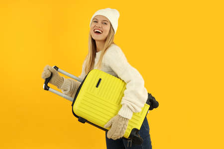Attractive girl in winter clothes with luggage bag on yellow background.の写真素材