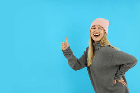 Attractive girl in sweater and knitted cap on blue background, space for text.