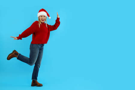 Attractive woman in sweater and Santa hat on blue background.の写真素材