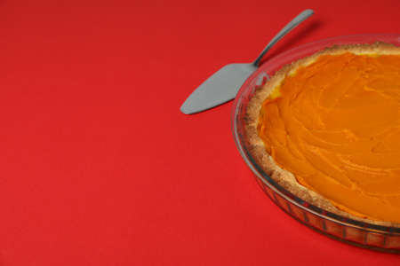 Pumpkin pie and cake spatula on red background