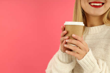 Attractive girl holds paper cup on pink background.