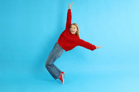 Attractive girl in sweater, jeans and sneakers on blue background.