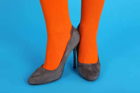 Female legs in orange socks and in heels on blue background