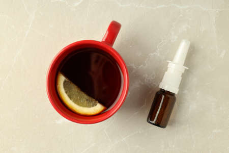 Blank bottle of nasal spray and cup of tea on light background