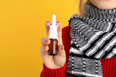 Young woman with nasal drops on yellow background, runny nose conceptの写真素材
