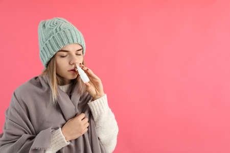 Young woman using nasal spray on pink background, runny nose conceptの写真素材
