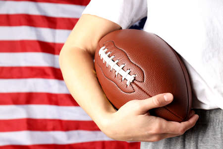 Woman holds American football ball on American flag backgroundの写真素材