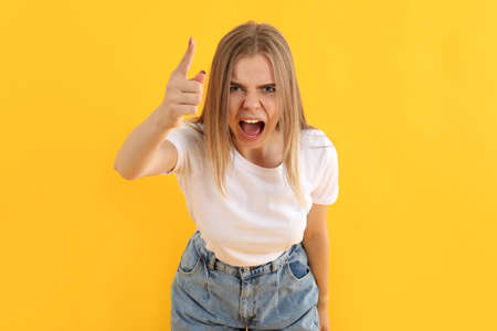 Young angry girl in jeans on yellow backgroundの写真素材