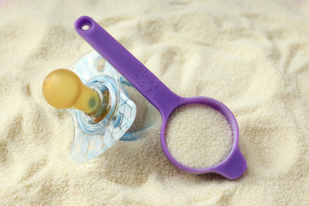 Pacifier and measuring spoon on powdered milk background