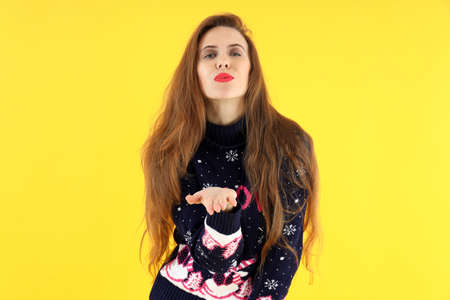 Attractive young woman in Christmas sweater on yellow background