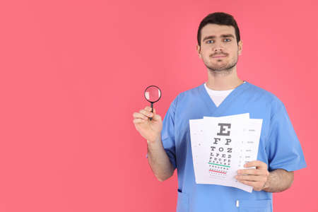 Male nurse holds magnifier and vision test on pink backgroundの写真素材