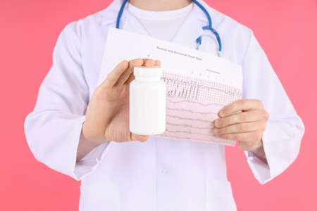 Doctor - intern holds cardiogram and bottle of pills on pink backgroundの写真素材