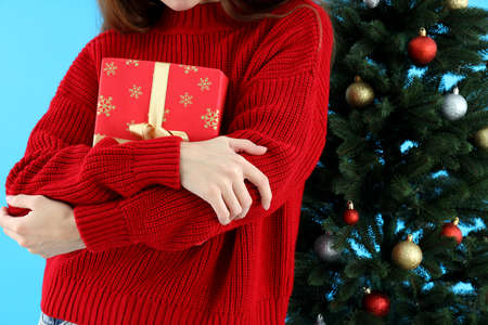 Woman holds gift box on blue background with Christmas treeの写真素材