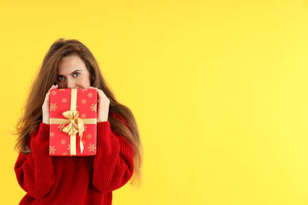 Attractive woman with Christmas gift box on yellow background