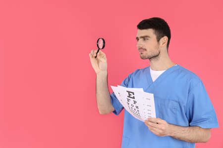 Male nurse holds magnifier and vision test on pink backgroundの写真素材