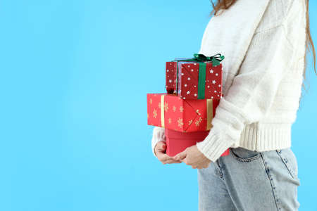 Woman in sweater holds gift boxes on blue backgroundの写真素材