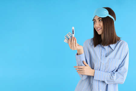 Attractive woman with pills and thermometer on blue background
