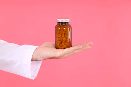 Hand of doctor hold bottle of pills on pink backgroundの写真素材