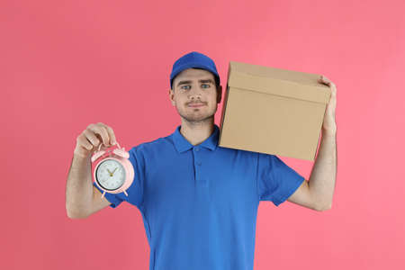 Delivery man holds box and alarm clock on pink backgroundの写真素材