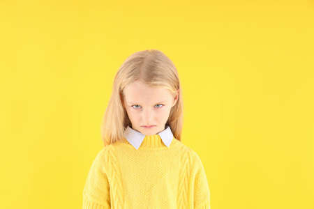 Angry little girl in sweater on yellow backgroundの写真素材