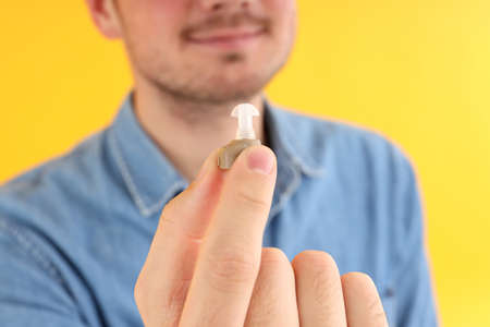 Young man hold hearing aid on yellow background