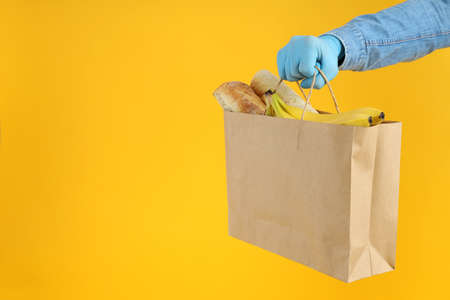 Hand in gloves hold bag with food on yellow backgroundの写真素材