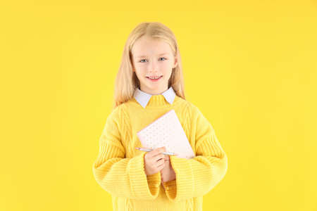 Cute little girl with notebook and pen on yellow backgroundの写真素材