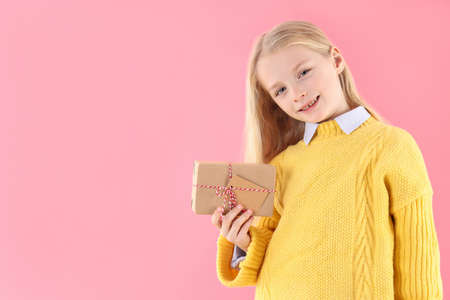 Cute little girl holds gift box on pink backgroundの写真素材