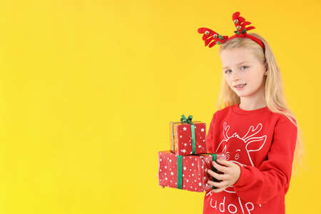 Little girl with Christmas boxes on yellow background