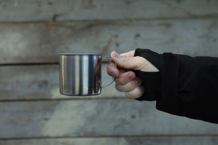 Male hand holds metal cup on wooden backgroundの写真素材