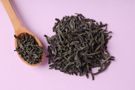 Spoon of black tea on purple background, top view