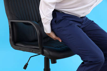 Man with bottom pain on blue background. Hemorrhoids conceptの写真素材