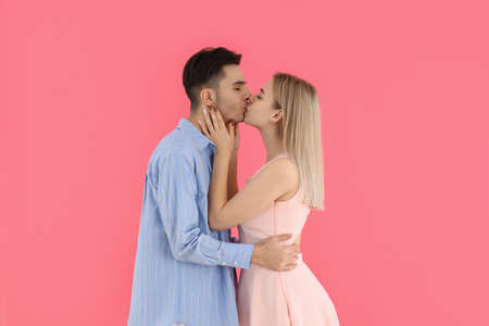 Cute and happy couple kissing on pink backgroundの写真素材