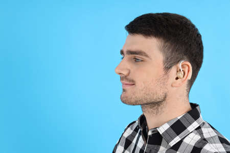 Young man with hearing aid on blue backgroundの写真素材