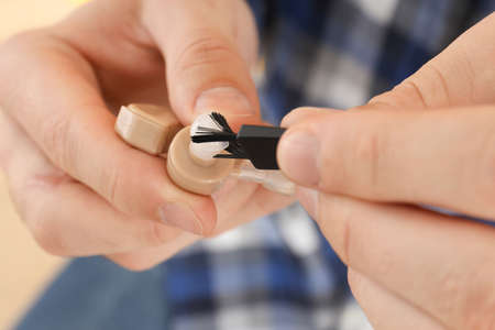 Young man cleans hearing aid, close up