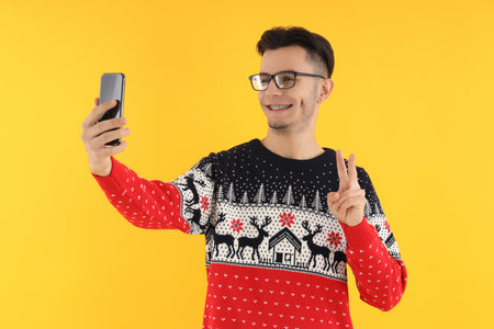 Guy in Christmas sweater with phone on yellow backgroundの写真素材